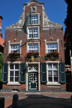 Fassade der historischen Weingroßhandlung J.W. Wolff, erbaut 1800, mit reich verziertem Backsteingiebel, grünen Fensterläden, goldener Schrift und detailreicher Eingangstür mit dekorativen Ornamenten.